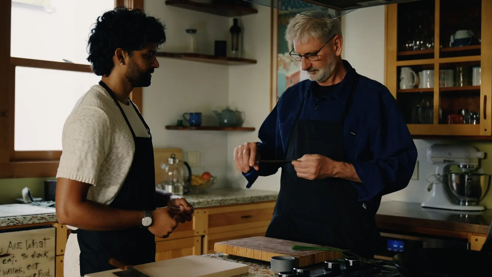 Akshay Prabhu hands a Chinese cleaver to a home cook in a sunlit kitchen