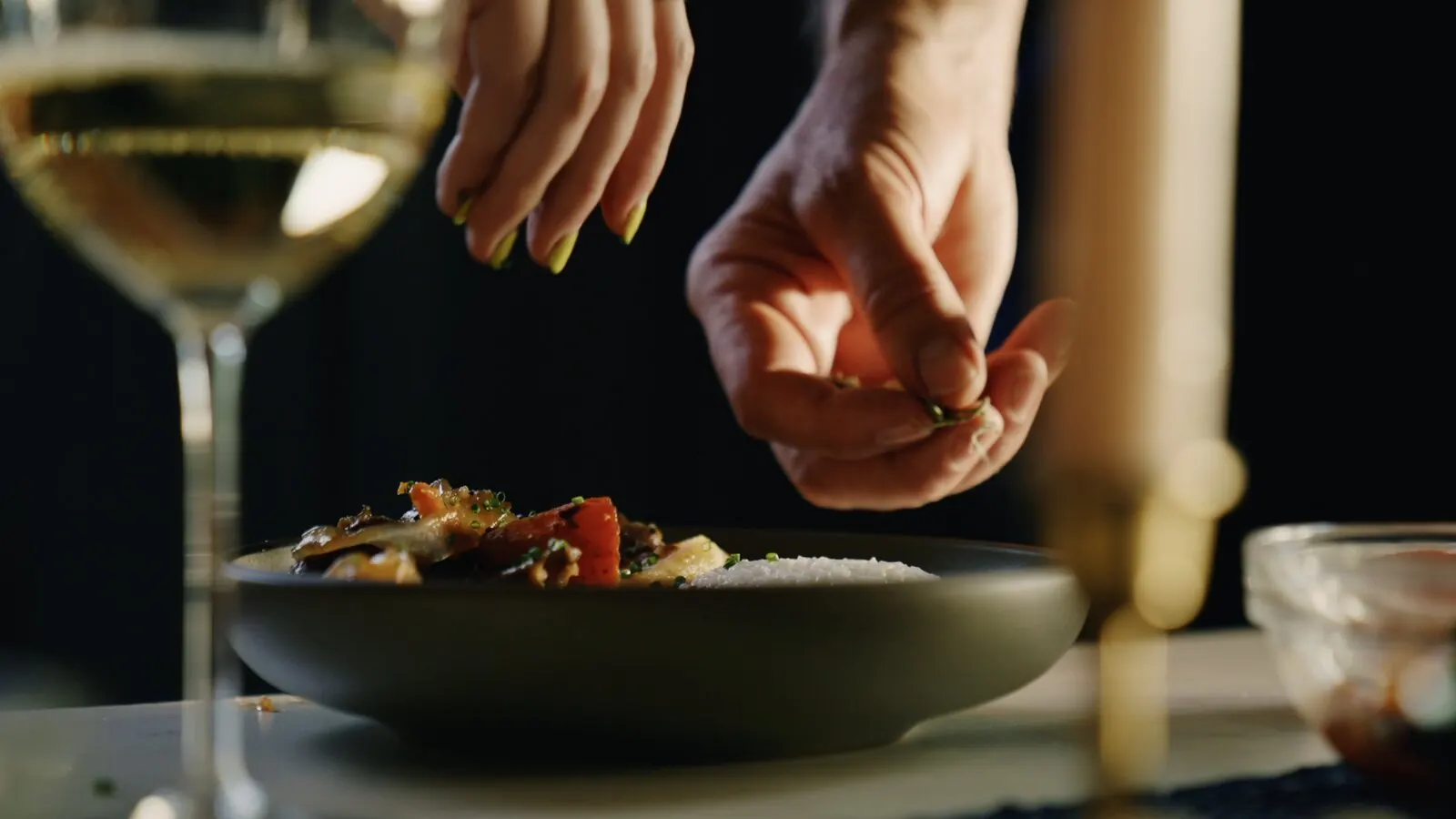 Hands finishing a plated stir-fry with fresh herbs