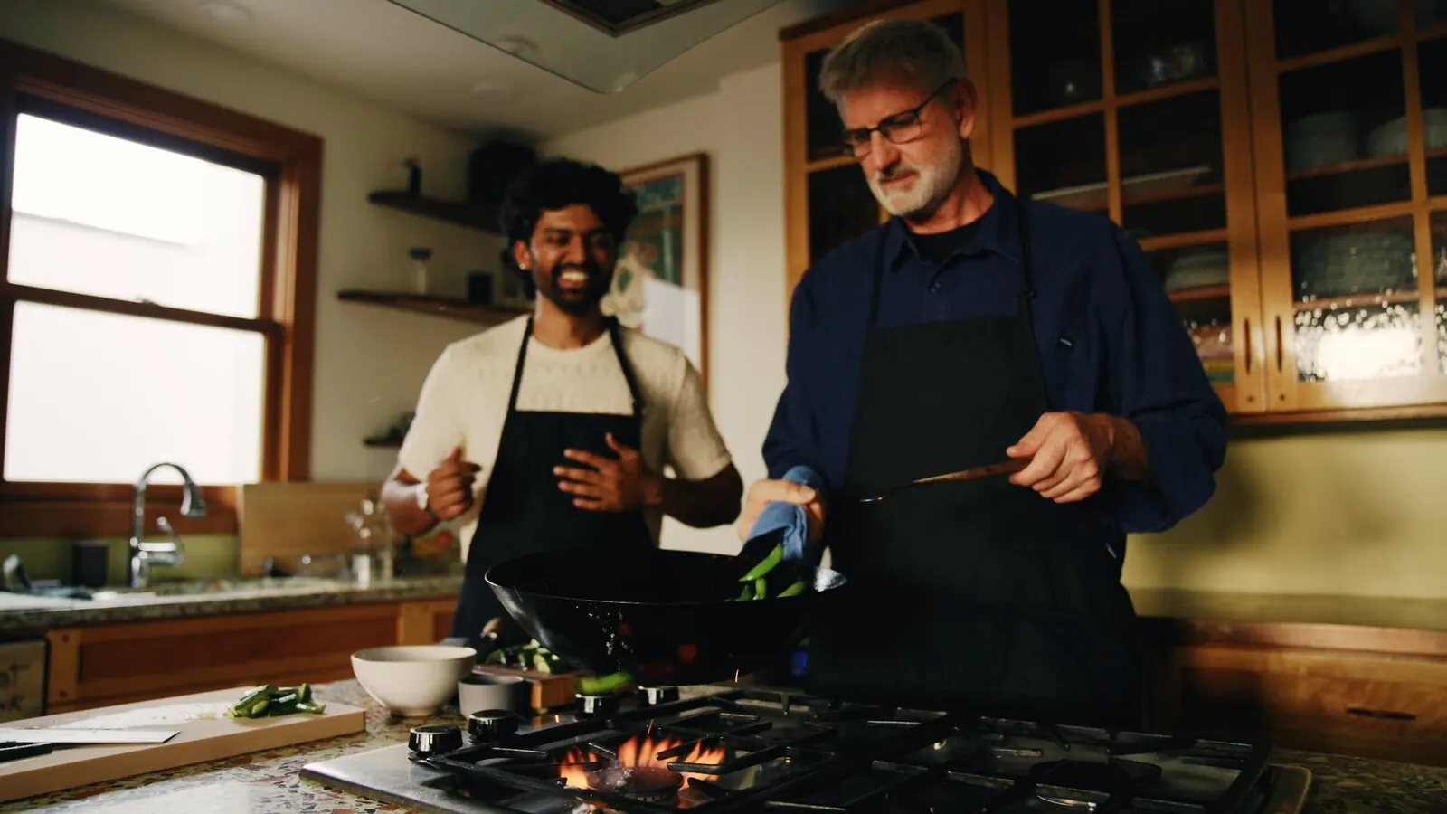 Akshay Prabhu laughs as a home cook tosses vegetables in a wok on a gas stove